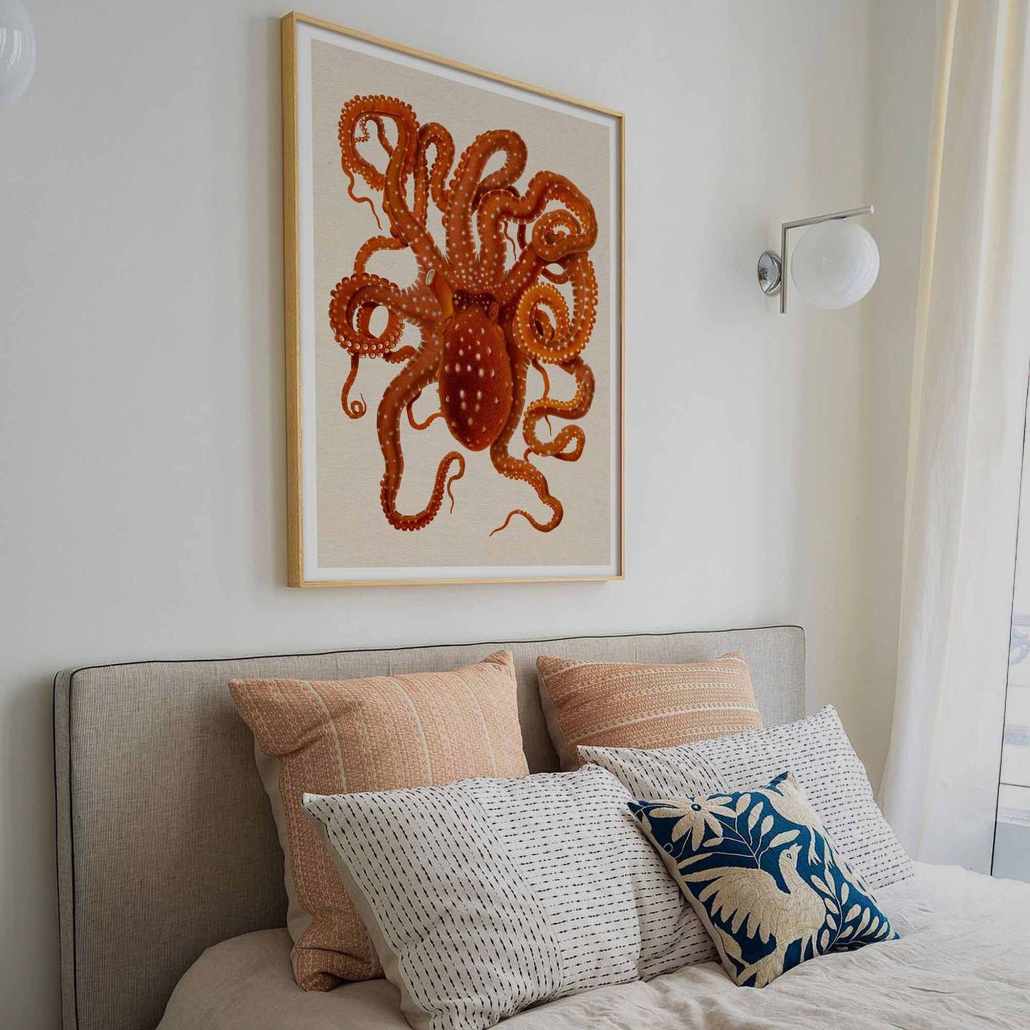 Vintage octopus illustration framed on a white wall above a cozy bed with decorative pillows in a soft, neutral-toned bedroom.
