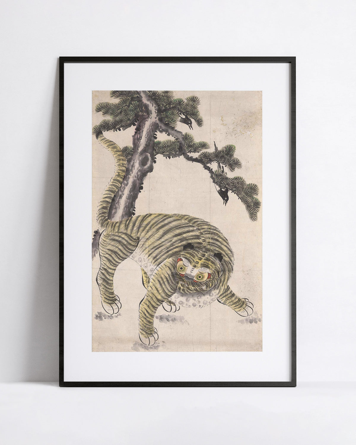 A framed art print featuring a traditional Korean-style illustration of a tiger crouching beneath a pine tree, displayed against a clean white wall.