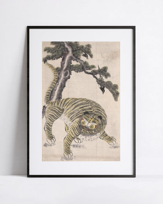 A framed art print featuring a traditional Korean-style illustration of a tiger crouching beneath a pine tree, displayed against a clean white wall.