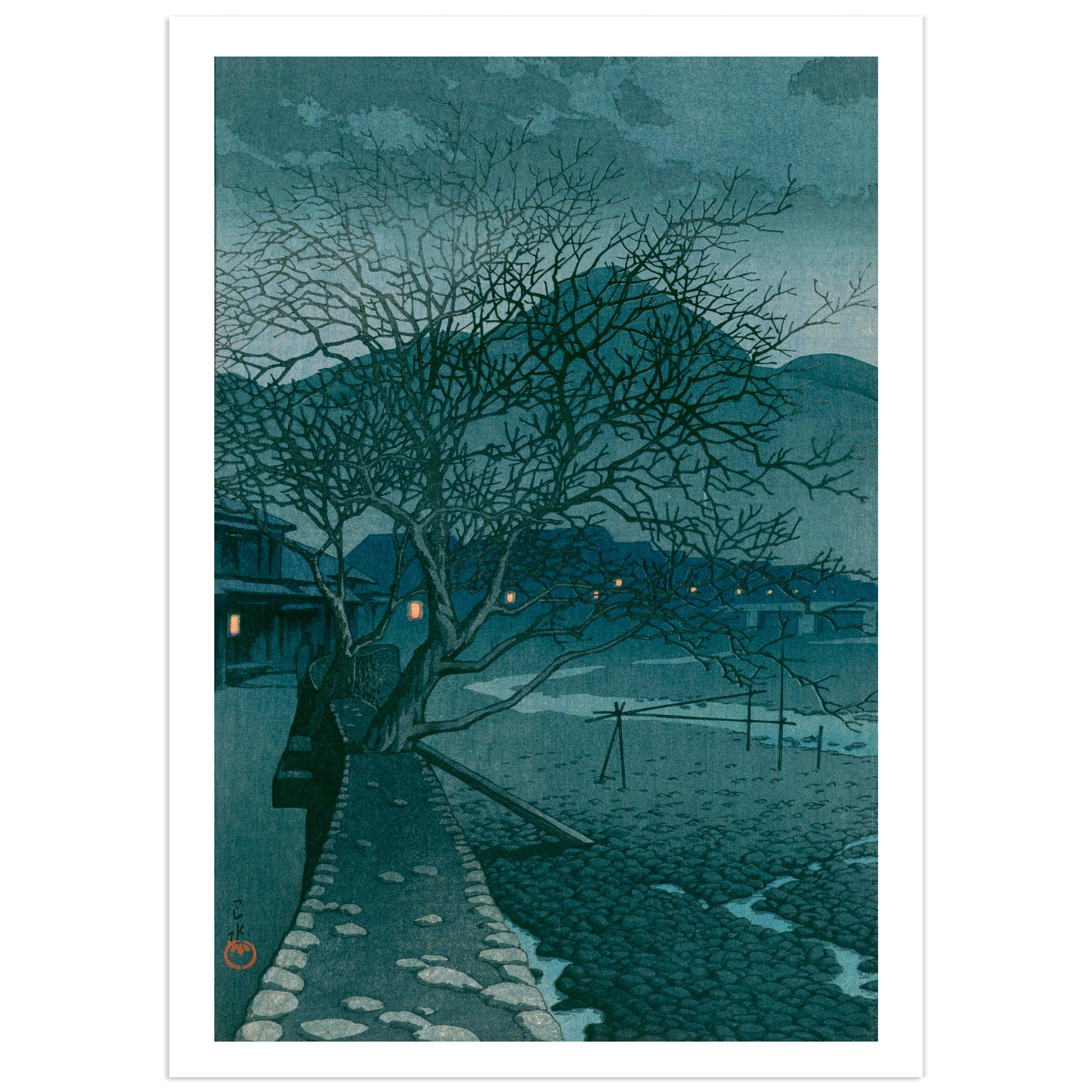 Japanese shin-hanga woodblock print by Kawase Hasui showing a stone path curving along a boulder-strewn riverbed at dusk in the hot-spring town of Beppu, with two bare winter trees overhead, blue hills behind, and small orange lantern lights glowing in the inns along the far bank.