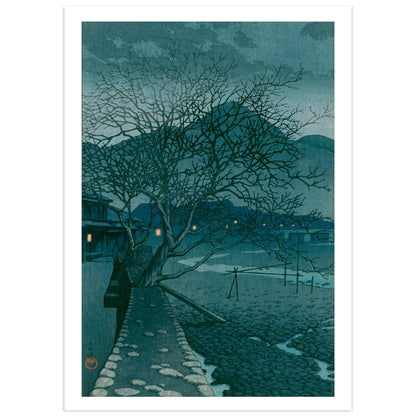 Japanese shin-hanga woodblock print by Kawase Hasui showing a stone path curving along a boulder-strewn riverbed at dusk in the hot-spring town of Beppu, with two bare winter trees overhead, blue hills behind, and small orange lantern lights glowing in the inns along the far bank.